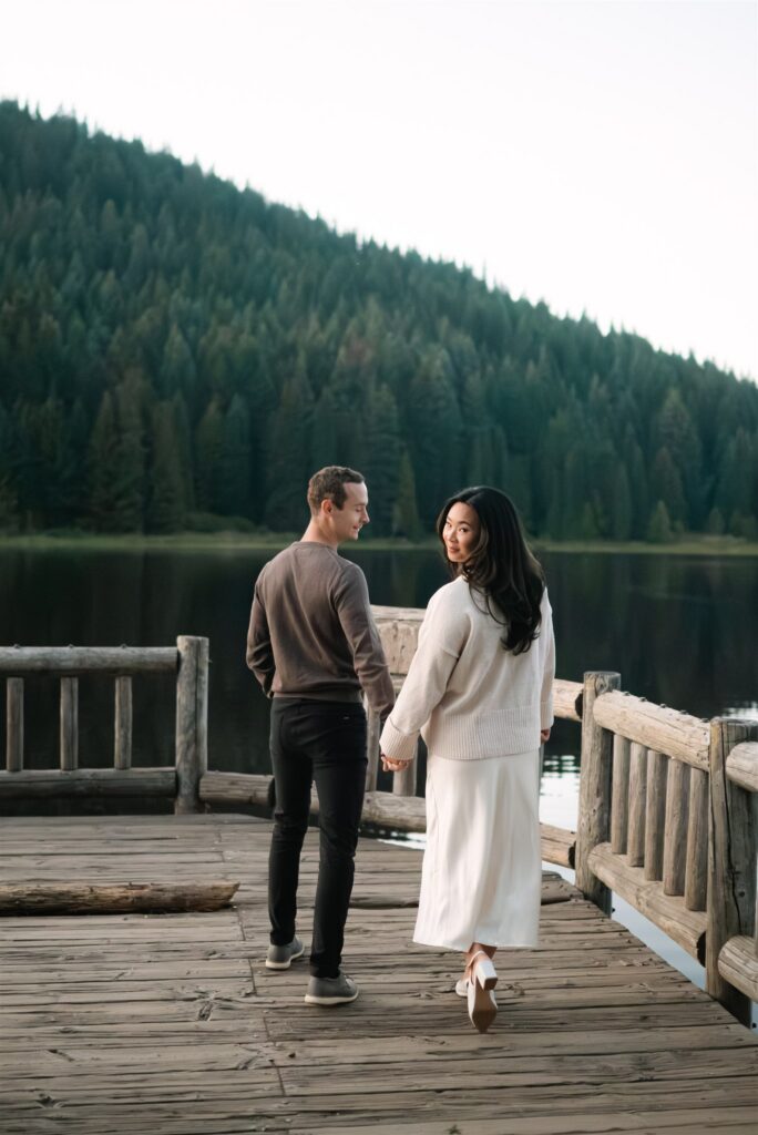Engaged couple walking together as the bride looks back smiling at the camera during their session