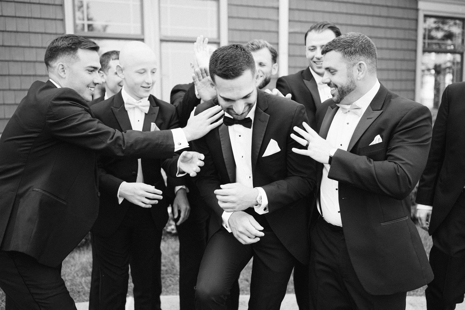 Groom laughing as his groomsmen playfully tussle him while getting ready on the wedding day