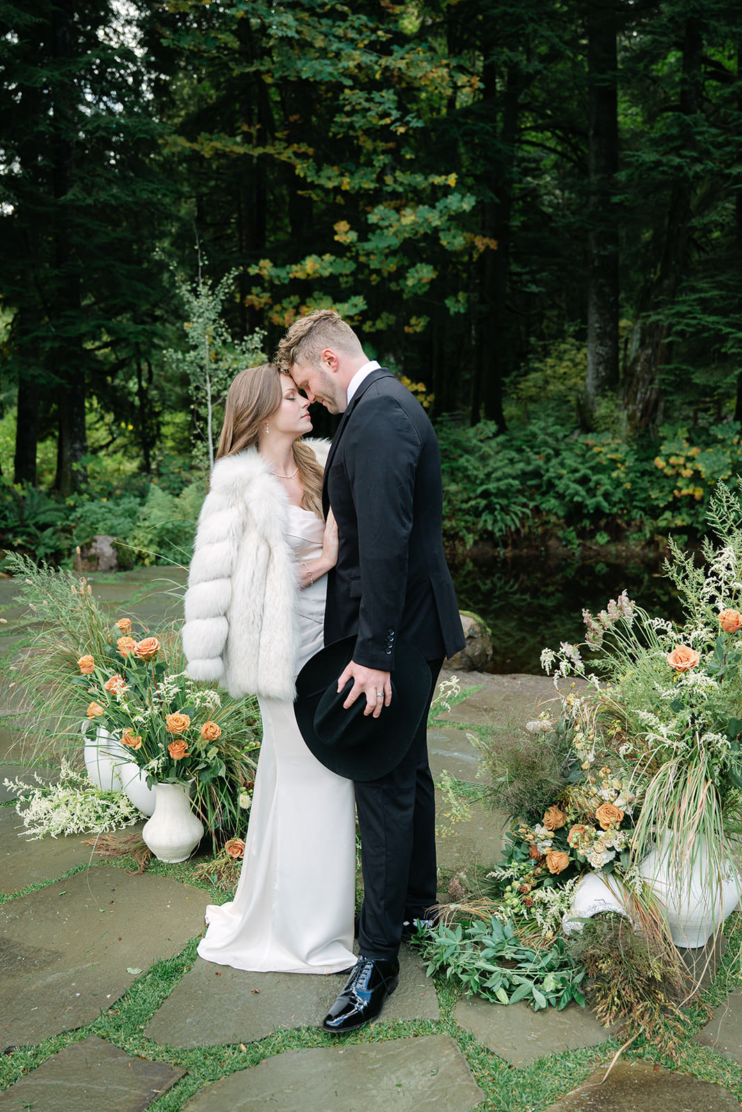 Bride and groom standing together in a garden setting with lush floral arrangements during their wedding portraits