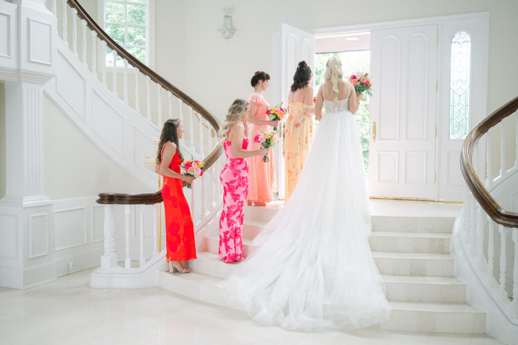 Bride in a ballgown standing with bridesmaids in mismatched floral dresses featuring red, yellow, and pink tones