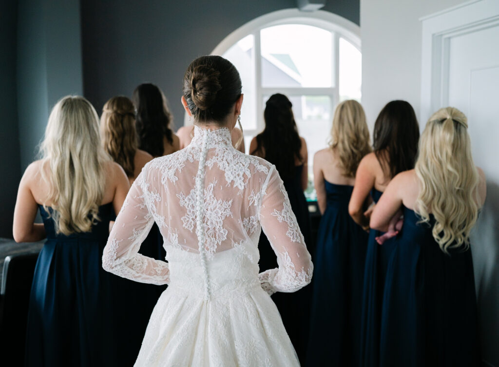 Bride Before Bridesmaid First Look Bride standing with her back turned before sharing a first look with her bridesmaids, showcasing the back of her wedding gown
